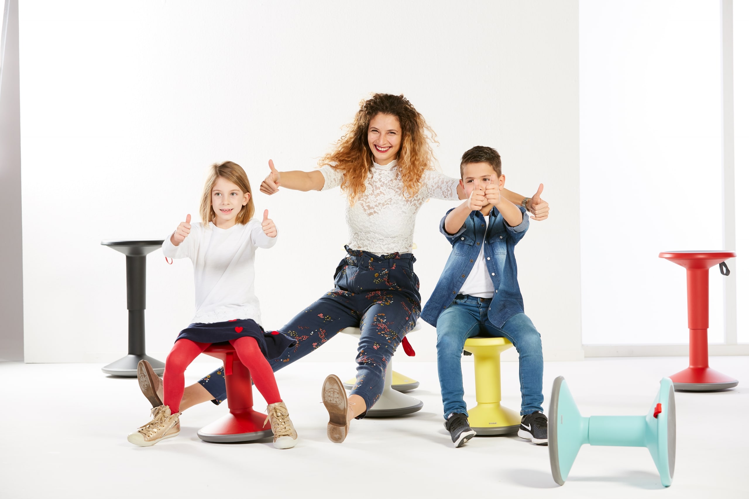 Hoogte verstelbare wiebelkruk voor kleuters, gebruikt door een vrouw en twee kinderen, met vrolijke kleuren en duimen omhoog.