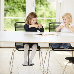 Concentratie Tafelschommel met kinderen die tekenen, zittend op moderne stoelen aan een lichte tafel in een rustige ruimte.