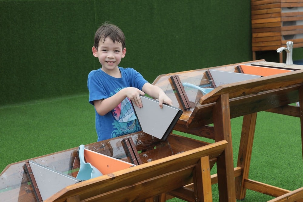 Kinderen spelen met de Waterbaan Outdoor XL, leren over waterstroming op een groene ondergrond.
