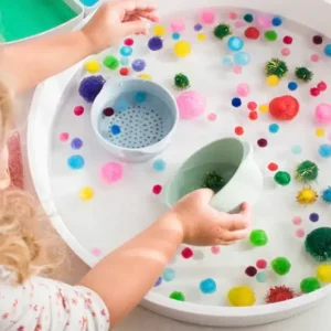 Nest schaaltjes in verschillende kleuren, gebruikt in een speelhoek met water en kleurrijke pompons.